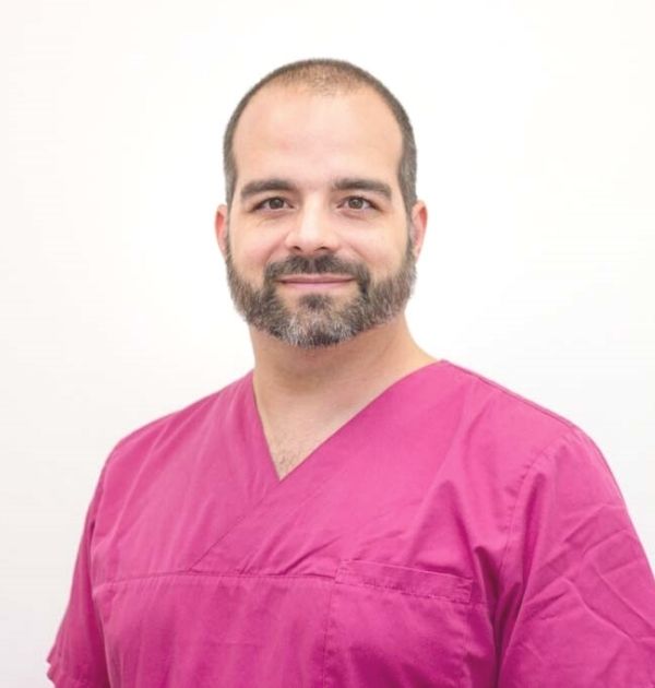 Zahnarzt Sebastian Koller mit magentafarbener Praxiskleidung